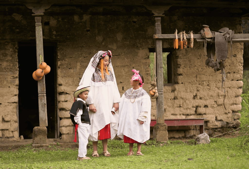 Niña y niños con vestimenta tradicional indígena en un entorno rural, símbolo de cultura y raíces ancestrales en México y América Central. – SoyMigrante.com REVISTA
