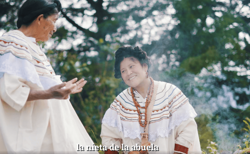 Niña de la abuela en celebración tradicional indígena en campo abierto, vestidas con ornamentos culturales, participando en ceremonia ancestral, reflejando identidad y cultura originaria en México. – SoyMigrante.com REVISTA