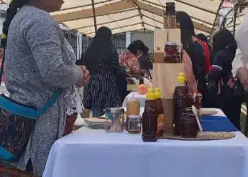 Botella de miel y productos artesanales en stand de feria cultural en un mercado al aire libre.