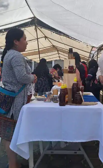 Botella de miel y productos artesanales en stand de feria cultural en un mercado al aire libre. – SoyMigrante.com REVISTA