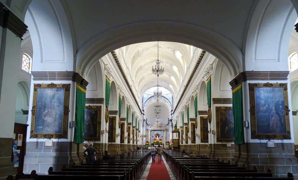 Imágenes de una iglesia o catedral con arquitectura clásica, altas bóvedas, pinturas religiosas y chandeliers en un ambiente luminoso y solemne. Ideal para contenido sobre cultura, historia y arte religioso. – SoyMigrante.com REVISTA