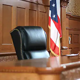 Silla de oficina en un despacho con bandera de EE.UU. en el fondo, ambiente formal y profesional, ideal para entrevistas, reuniones legales o actividades judiciales. – SoyMigrante.com REVISTA