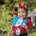 Niña con vestimenta tradicional y bandera de Guatemala, sonriendo feliz en un entorno natural, símbolo de cultura, identidad y orgullo en el contexto migrante. – SoyMigrante.com REVISTA