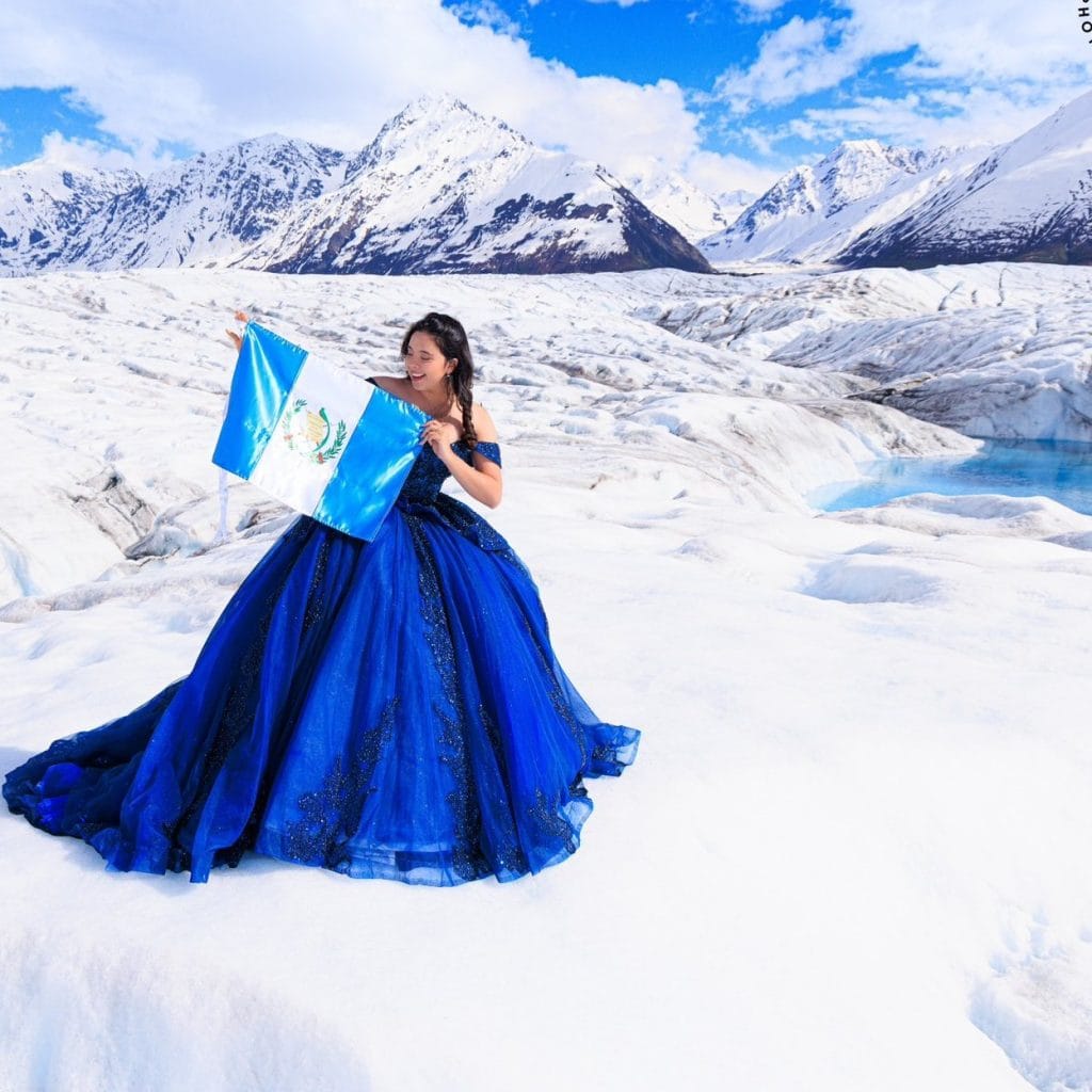 Hermosa joven con vestido azul en paisaje glaciar, representando la cultura guatemalteca y la migración en un escenario natural de glaciares.