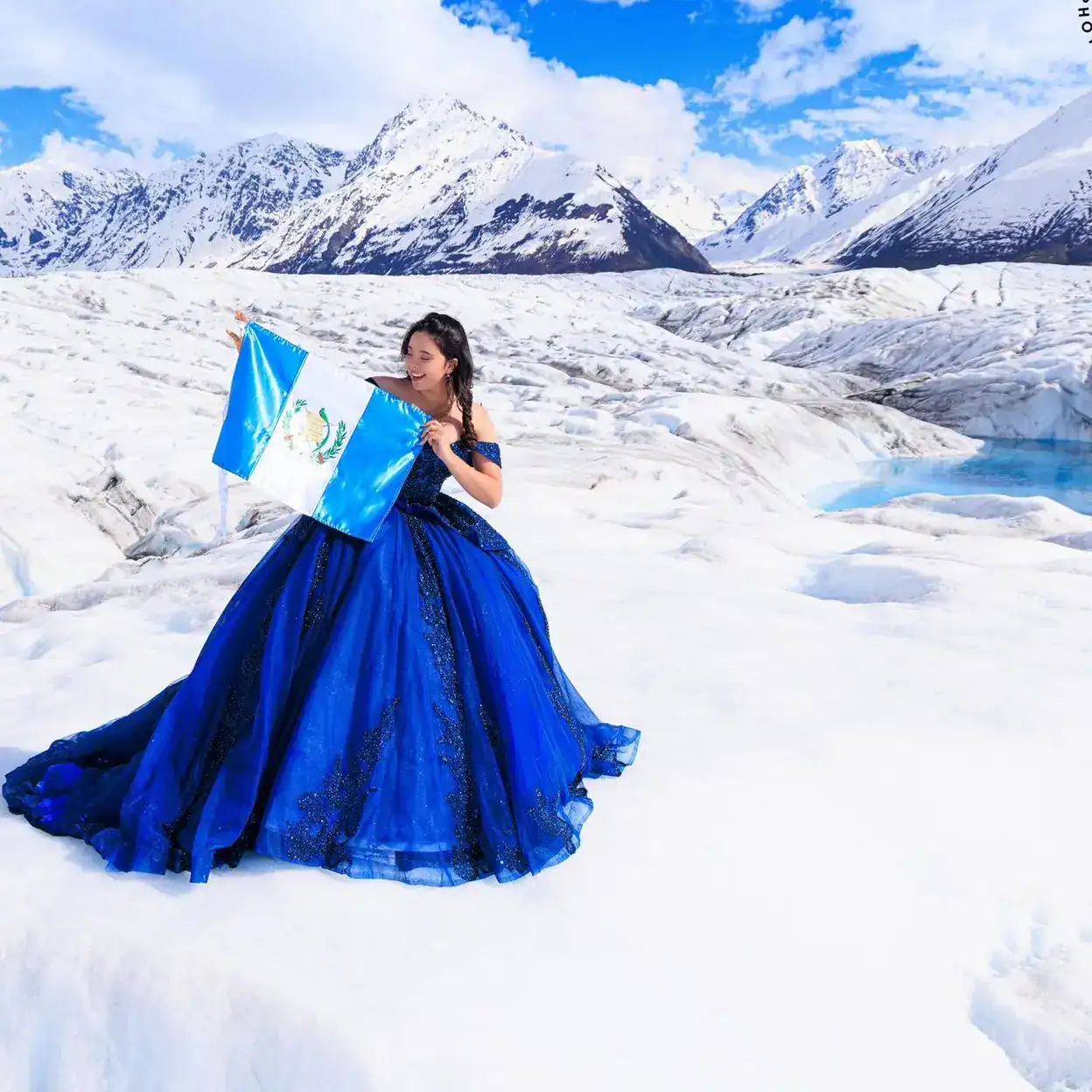 Hermosa joven con vestido azul en paisaje glaciar, representando la cultura guatemalteca y la migración en un escenario natural de glaciares.