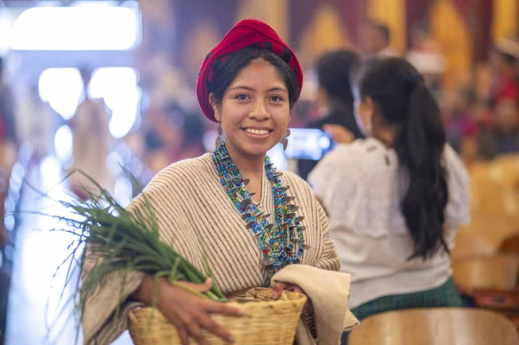 Artesana indígena mexicana con vestimenta tradicional y accesorios coloridos en un mercado cultural, promoviendo la identidad y el turismo en México.