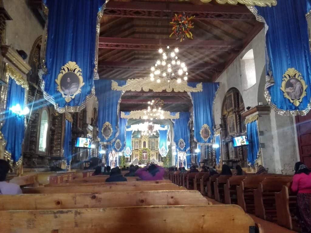 Colores vibrantes en la decoración de una iglesia tradicional con candelabros y altares ornamentados, reflejando cultura y fe en un entorno eclesiástico. – SoyMigrante.com REVISTA