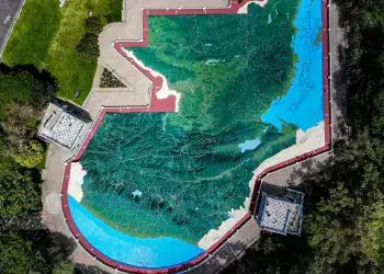 Jardín con mural de mapa topográfico pintado en el suelo, rodeado de áreas verdes y caminos, en un lugar público y cultural, promoviendo la educación ambiental y el arte al aire libre. – SoyMigrante.com REVISTA