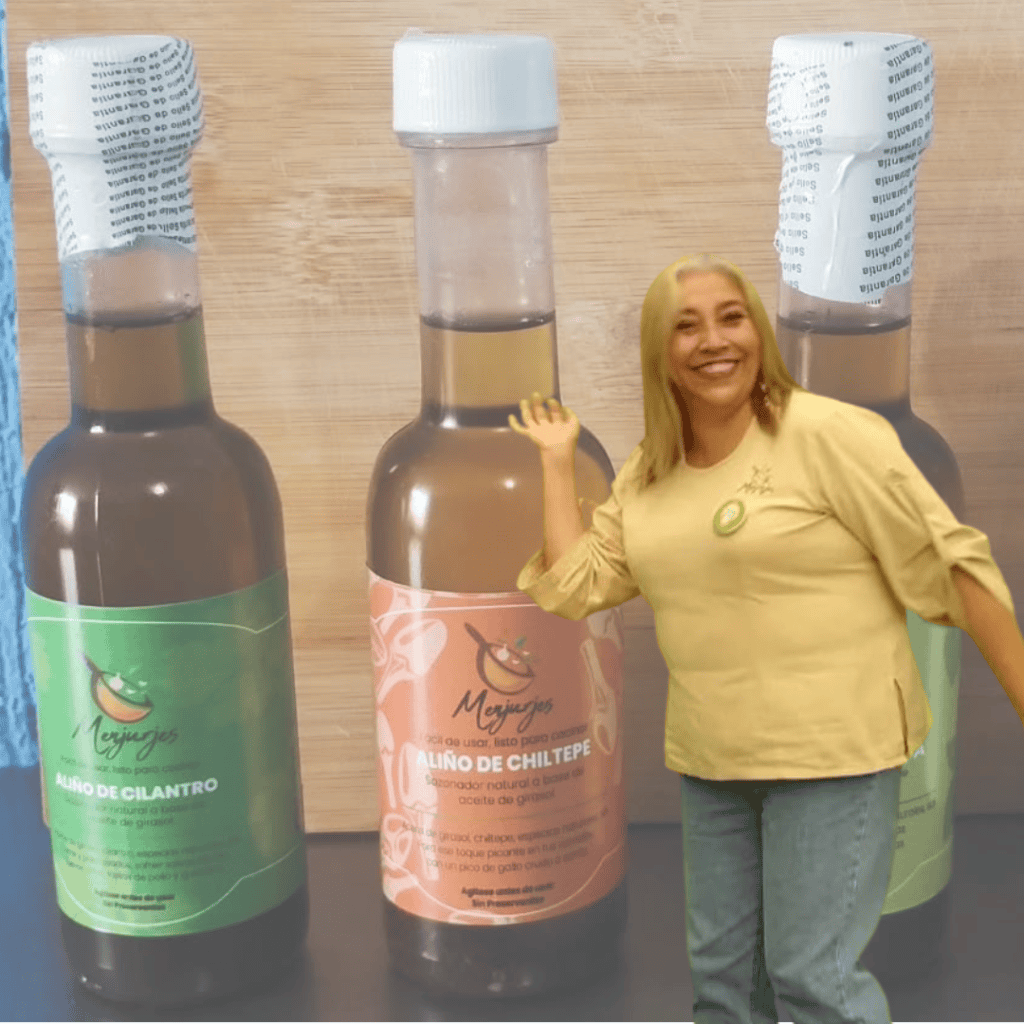 Aceite de cilantro y chile de Chilete en botellas grandes con etiquetado de SoyMigrante.com revista, mujer sonriente en fondo de madera mostrando productos tradicionales de la gastronomía peruana.