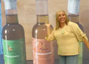 Aceite de cilantro y chile de Chilete en botellas grandes con etiquetado de SoyMigrante.com revista, mujer sonriente en fondo de madera mostrando productos tradicionales de la gastronomía peruana.