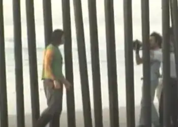 mojado ricardo arjona (2) – SoyMigrante.com REVISTA Migrantes frente a barrera de metal en frontera, buscando ingreso o salida, situación común en migración y derechos humanos, en contexto de migrantes en movimiento.