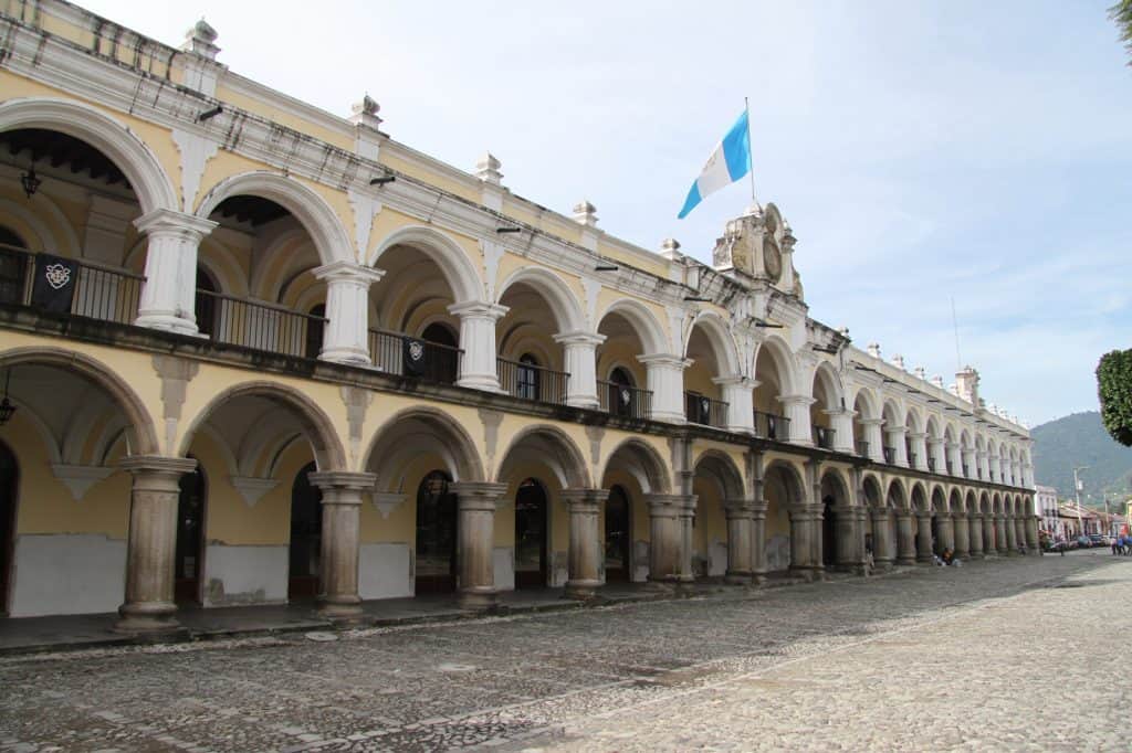 Elegante edificio colonial en Guatemala con arcos y columnas, símbolo del patrimonio y cultura local, destacado en la revista SoyMigrante.com REVISTA, ideal para artículos sobre migración, historia y turismo en Centroamérica. – SoyMigrante.com REVISTA