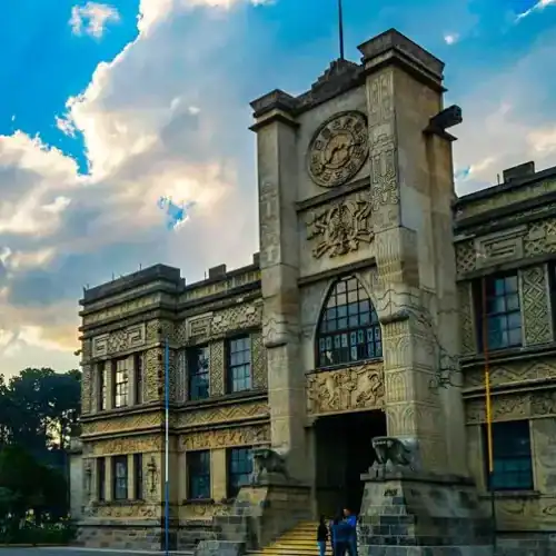 Edificio histórico con reloj en fachada y detalles arquitectónicos ornamentales, en un día soleado con cielo parcialmente nublado en la ciudad. – SoyMigrante.com REVISTA