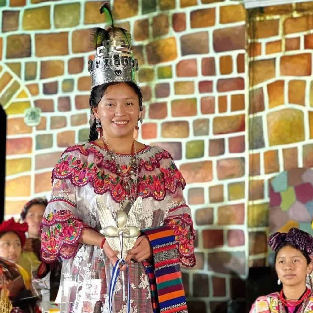 Vestido tradicional indígena con ornamentos y tocado de plumas, mujer en evento cultural de comunidad originaria en México, celebrando su identidad y patrimonio cultural. – SoyMigrante.com REVISTA