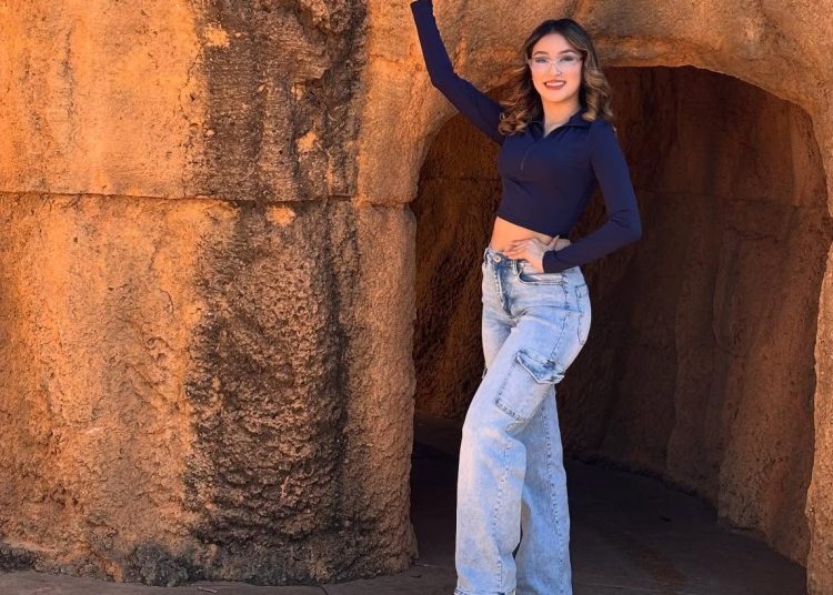 Joven mujer con gafas y jeans anchos en un entorno rocoso, promocionando la revista SoyMigrante.com REVISTA, destacando cultura migrante y fotografía de viaje para comunidad hispanohablante. – SoyMigrante.com REVISTA