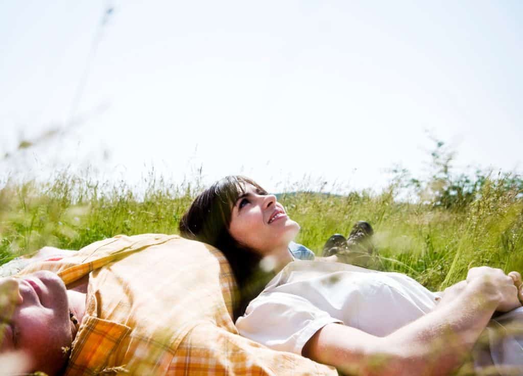 Joven mujer disfrutando del campo al aire libre, descansando sobre la hierba en un día soleado, promoviendo bienestar, naturaleza y salud.