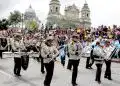 Jóvenes músicos militares tocando instrumentos en una plaza concurrida con una multitud y un edificio histórico en el fondo.
