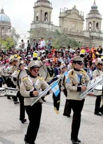 Jóvenes músicos militares tocando instrumentos en una plaza concurrida con una multitud y un edificio histórico en el fondo.