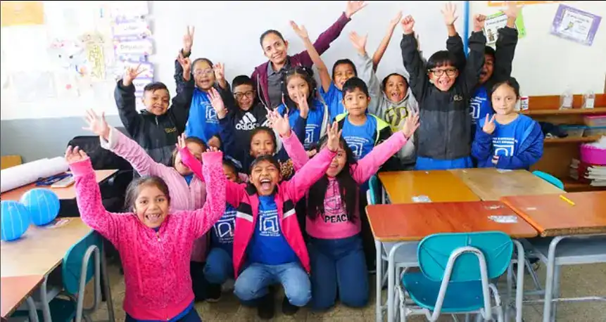 Mejorando la educación de niños migrantes en clase interactiva, con profesores y estudiantes felices en un aula colorida y motivadora, promoviendo integración y crecimiento cultural. – SoyMigrante.com REVISTA