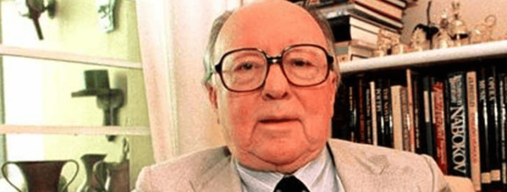 Hombre mayor con gafas y chaqueta en interior con libros de fondo en una estantería, imagen relacionada con cultura y migrantes, en el contexto de SoyMigrante.com REVISTA. – SoyMigrante.com REVISTA