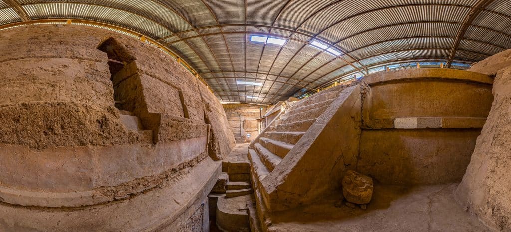 Antiguas escaleras y muros de piedra en un sitio arqueológico, protegido con techumbre metálica, en un contexto de historia y cultura prehispánica mexicana. – SoyMigrante.com REVISTA