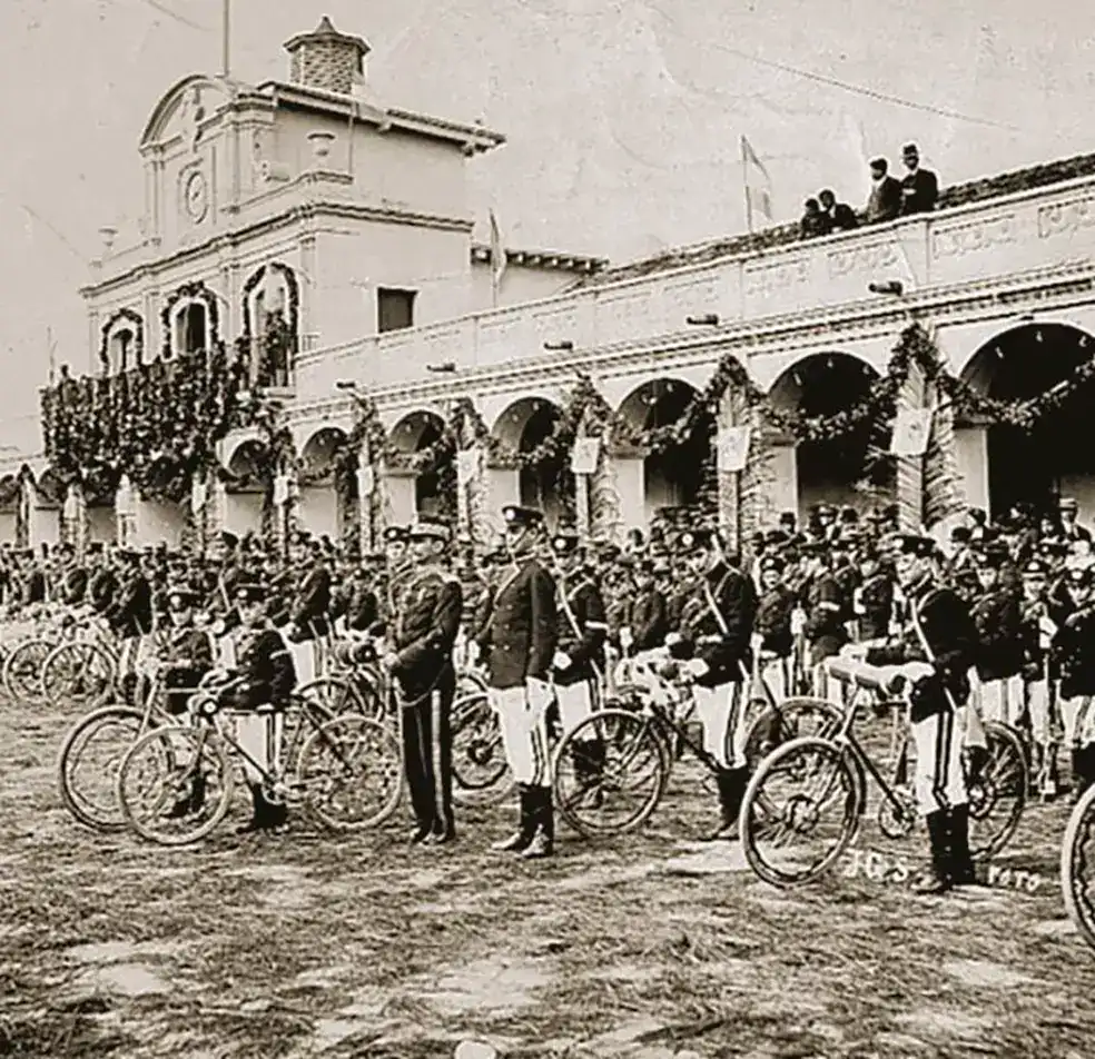 Niños y adultos en una celebración en la plaza principal, con un edificio histórico decorado con guirnaldas y banderas, en una imagen antigua que destaca la cultura y tradiciones locales. – SoyMigrante.com REVISTA
