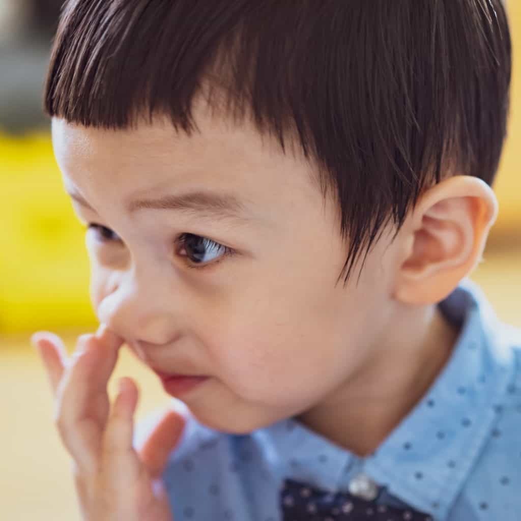 Por qué es tan dañino para la salud picarse la nariz o introducir objetos 1 – SoyMigrante.com REVISTA Niño pequeño con expresión curiosa, tocándose la cara, en un entorno educativo, promoviendo temas de infancia y aprendizaje.