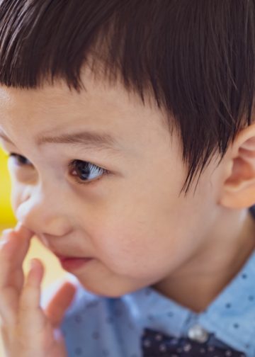 Por qué es tan dañino para la salud picarse la nariz o introducir objetos 1 – SoyMigrante.com REVISTA Niño pequeño con expresión curiosa, tocándose la cara, en un entorno educativo, promoviendo temas de infancia y aprendizaje. – SoyMigrante.com REVISTA