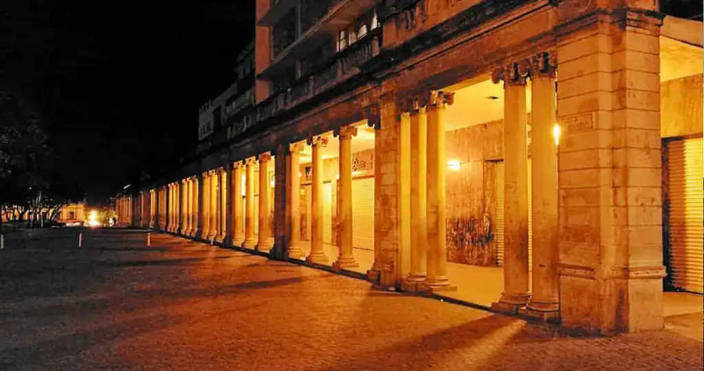 Farolas iluminando un edificio con columnas en la noche, imagen de revista SoyMigrante.com, ideal para temas de migración, cultura y comunidad en contextos urbanos y mundiales. – SoyMigrante.com REVISTA