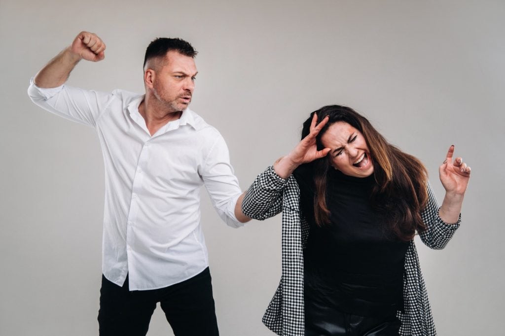 Un hombre agrediendo a una mujer en una discusión, mostrando tensión y conflicto, en un fondo neutral.