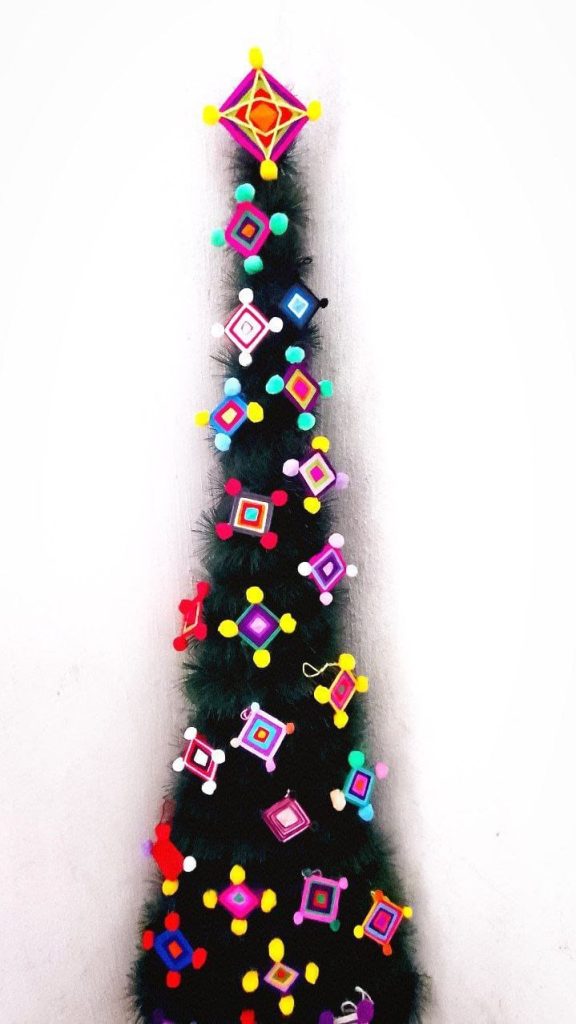 Colgante decorativo de Navidad con diversos colores y formas geométricas en forma de estrellas y cuadrados, elaborado con filamentos de colores y pompones, ideal para adornar en festividades. – SoyMigrante.com REVISTA
