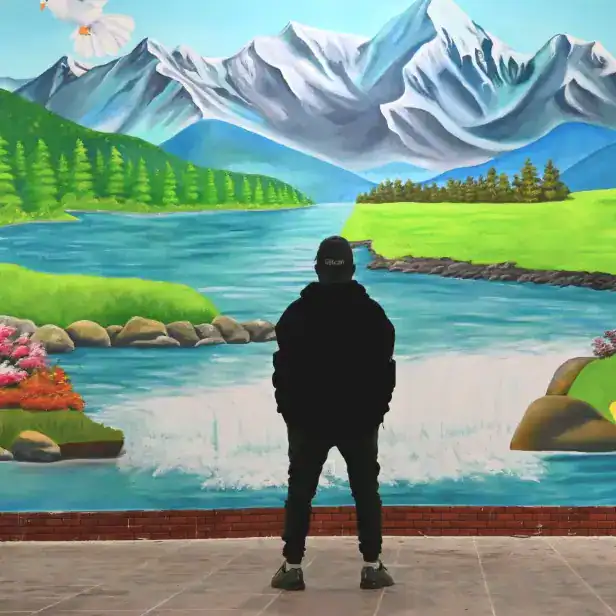Paisaje pintado de montañas, río y naturaleza con persona observando mural artístico en la revista SoyMigrante.com. – SoyMigrante.com REVISTA