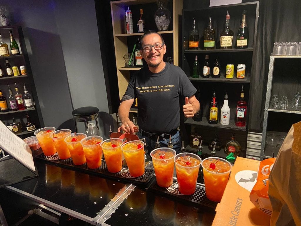 Refresco de cóctel tropical preparado por bartender en bar de estilo moderno con botellas de licor en estanterías. – SoyMigrante.com REVISTA