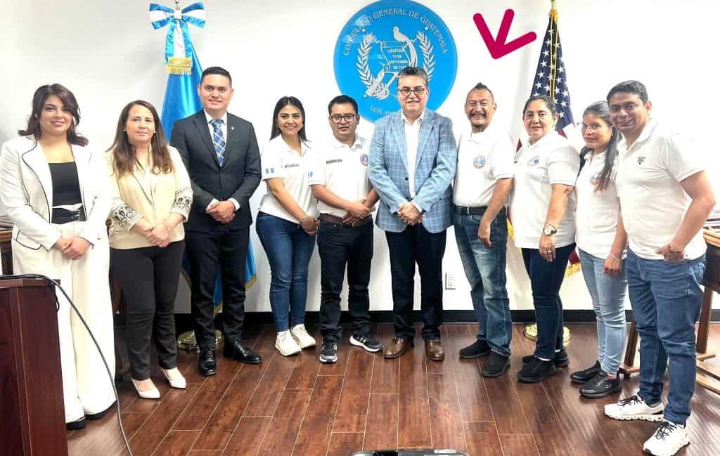 Guatemaltecos en una reunión oficial, con el logo de la Coordinadora General de Guatemala y banderas, promoviendo la comunidad y el apoyo en temas de migración y derechos humanos en Guatemala. – SoyMigrante.com REVISTA