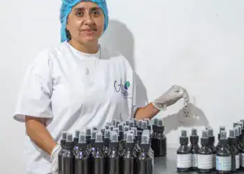 Botellas de productos cosméticos en un laboratorio de fabricación, mujer trabajando con ética en el sector cosmético, innovación en la industria de belleza para emigrantes en Latinoamérica.