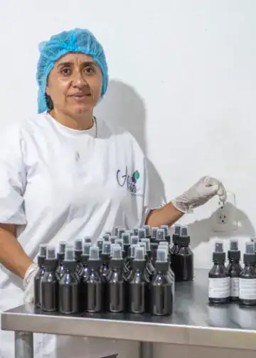 Botellas de productos cosméticos en un laboratorio de fabricación, mujer trabajando con ética en el sector cosmético, innovación en la industria de belleza para emigrantes en Latinoamérica.
