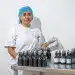 Botellas de productos cosméticos en un laboratorio de fabricación, mujer trabajando con ética en el sector cosmético, innovación en la industria de belleza para emigrantes en Latinoamérica.