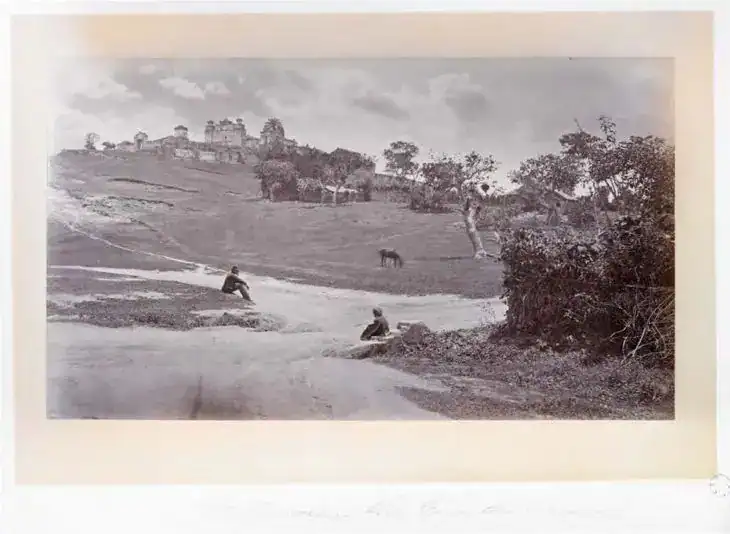 Camino rural en país agrícola antiguo con campesinos trabajando, árboles y casas en colina, imagen histórica en blanco y negro, reflejando la vida rural mexicana.