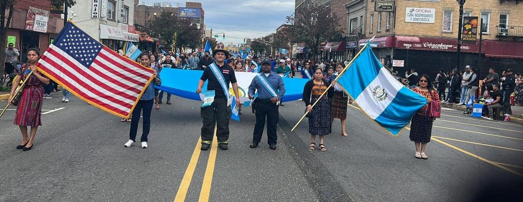 Estados Unidos y Guatemala en una marcha cultural, portando banderas en una celebración multitudinaria en la calle, mostrando diversidad y orgullo hispano en un evento comunitario. – SoyMigrante.com REVISTA