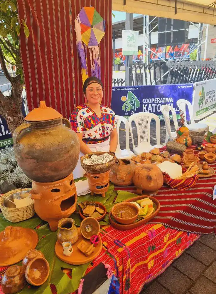 Vendedora en puesto de artesanías y cerámica tradicional mexicana en feria cultural con decoraciones coloridas y productos artesanales en el stand. – SoyMigrante.com REVISTA