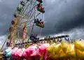 Niños disfrutando en la feria con una noria gigante y puestos con algodón de azúcar, en un día con nubes oscuras, en la revista SoyMigrante.com REVISTA, que habla sobre experiencias y cultura migrante.