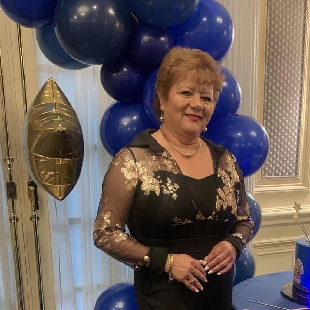 Celebración con globos azules y dorados, mujer vestida con elegante atuendo con detalles dorados, en evento especial destacado en Revista SoyMigrante.com.