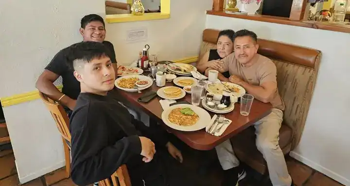 Disfrutando una comida en familia en un restaurante, en un ambiente acogedor y amistoso, promoviendo la cultura hispana y la importancia de la comunidad en el contexto de migración y vida en el extranjero. – SoyMigrante.com REVISTA