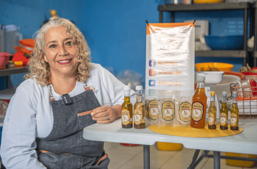 Aceite artesanal y productos naturales en la feria gastronómica de SoyMigrante.com REVISTA, con mujer emprendedora mostrando ingredientes y aceites en un ambiente de cocina o mercado. – SoyMigrante.com REVISTA