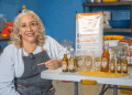 Aceite artesanal y productos naturales en la feria gastronómica de SoyMigrante.com REVISTA, con mujer emprendedora mostrando ingredientes y aceites en un ambiente de cocina o mercado. – SoyMigrante.com REVISTA