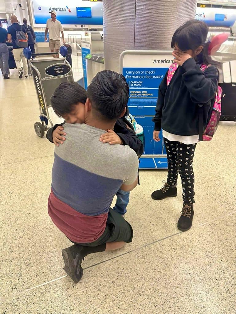 Un familiar de dos niños se despide de ellos poco antes de que aborden un vuelo hacia Guatemala para reunirse con su mamá, que fue deportada. (Foto Guatemalan Maya Center) – SoyMigrante.com REVISTA