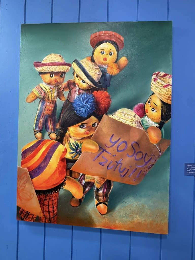 Yo soy Tzutujil, es el expresivo título de esta pintura de Dominick Cocozza, en la cual muñequitos tradicionales guatemaltecos se convierten en protagonistas de un reconocimiento de identidad. (Foto Nacho Méndez) – SoyMigrante.com REVISTA