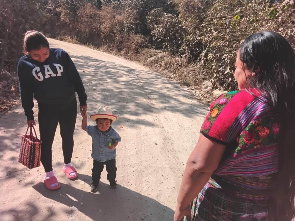 Gloria se encuentra con una de sus hijas y su nieto Caleb, en el camino de Hacienda Vieja hacia San José Poaquíl: un camino de tiempos que le llevó de niña a huir, de adolescente a volver, de adulta a ver partir a su esposo Gabriel como migrante y también a ir al aeropuerto a traerlo para seguir construyendo más camino. (Foto Gustavo Montenegro)