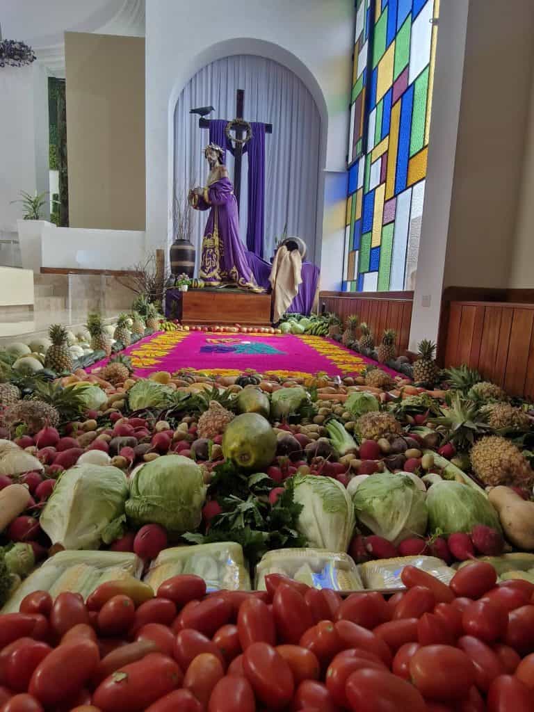 Sin la cruz a cuestas que llevará el Viernes Santo, los Nazarenos suelen aparecer en el momento de la oración en el Huerto: sí, ese mismo huerto que se representa con frutas, verduras, aserrín, flores y sobre todo: amor. Huerto en parroquia Cristo Rey, zona 15, Guatemala.