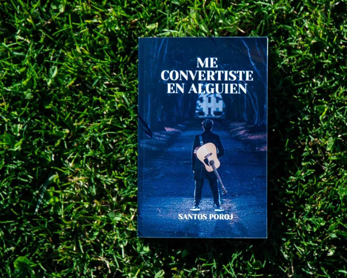 Blue book cover on grass with the title 'Me convertiste en alguien' and a person with a guitar pictured on the cover.